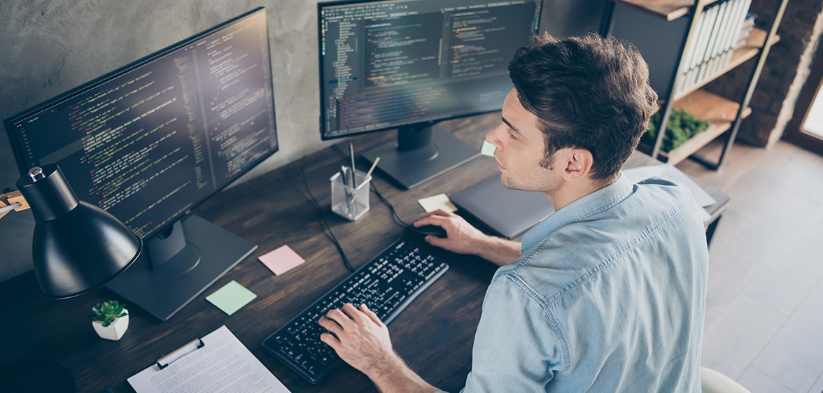 Szoftverfejlesztő Egy programozó ül egy íróasztalnál és két monitor van előtte amin dolgozik.